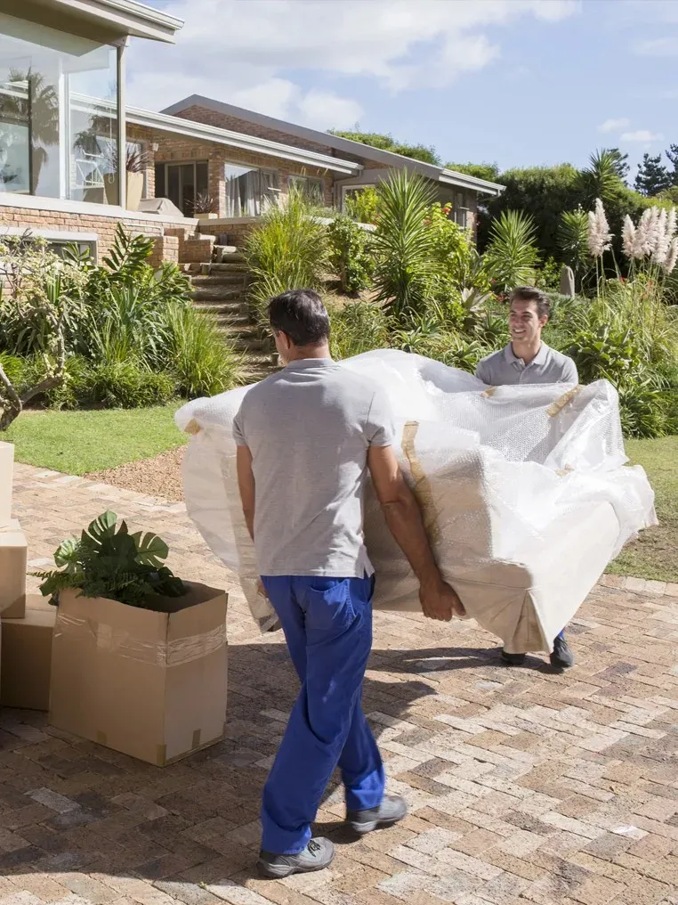 Umzugshelfer tragen ein verpacktes Sofa zum Haus