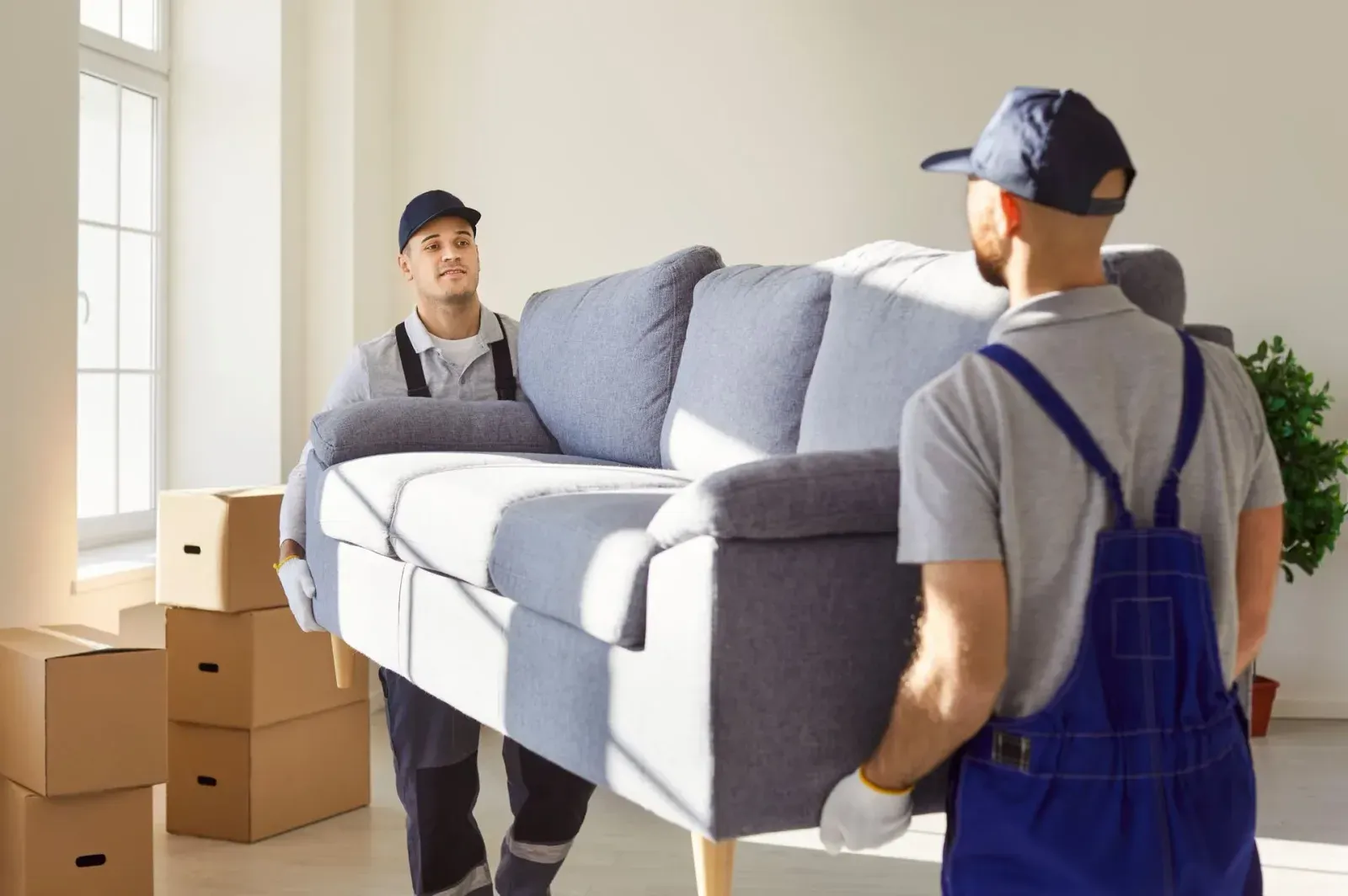 Zwei Umzugshelfer tragen ein Sofa durch die leere Wohnung